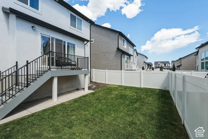 Rear exterior featuring a raised deck with black railings, sliding glass doors, white stucco siding, and a manicured lawn