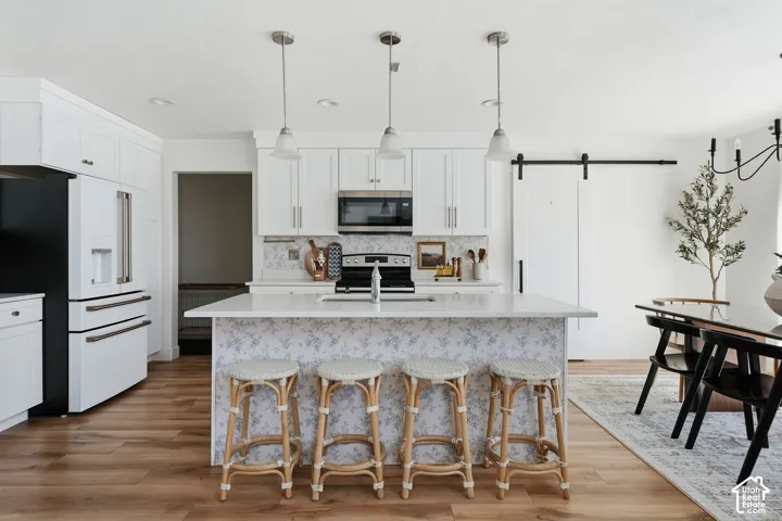 Spacious kitchen featuring white cabinetry, light wood-finish flooring, a patterned tile backsplash, and a large central island with an integrated sink