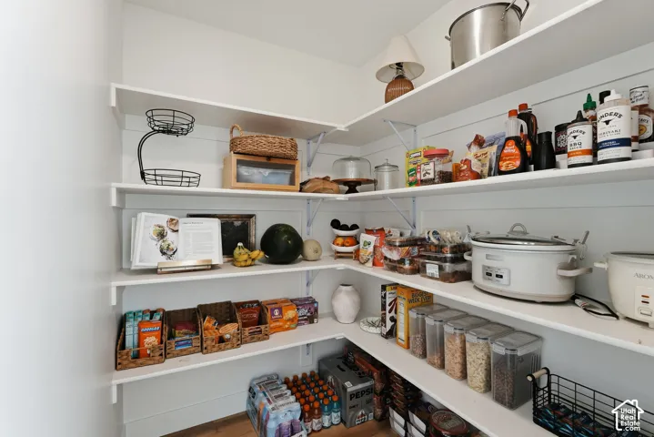 Walk-in pantry featuring white shelving, shiplap-style wall paneling, and wood-finish flooring