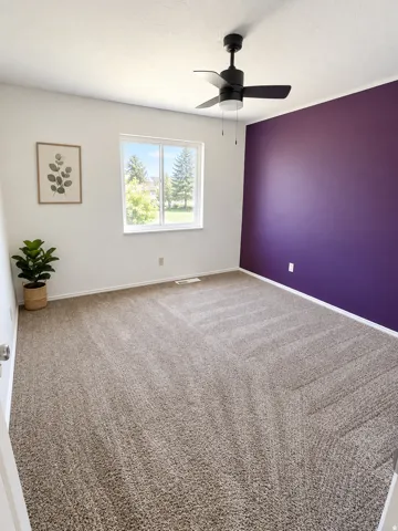 Wall-to-wall carpeting, white walls, accent wall, ceiling fan with light fixture, and window