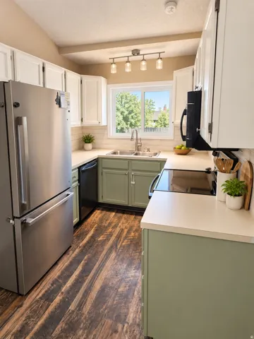 Kitchen featuring wood-finish flooring, stainless steel appliances, a tile backsplash, track lighting, and a vaulted ceiling