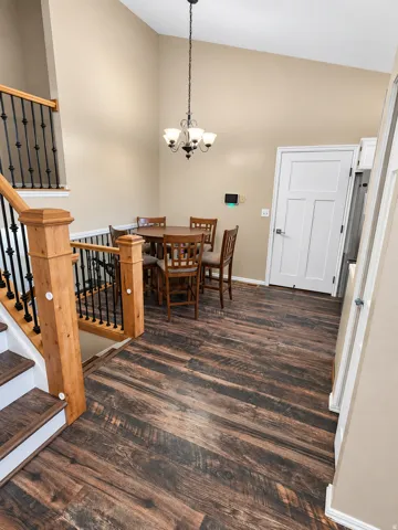 Vaulted ceiling with a chandelier, wood-finish flooring, staircase with wood newel posts and wrought iron balusters, and a paneled interior door