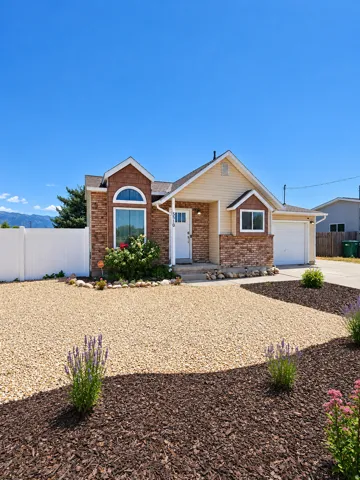 Brick and siding exterior, arched window, attached garage, white fencing, and rock and mulch landscaping