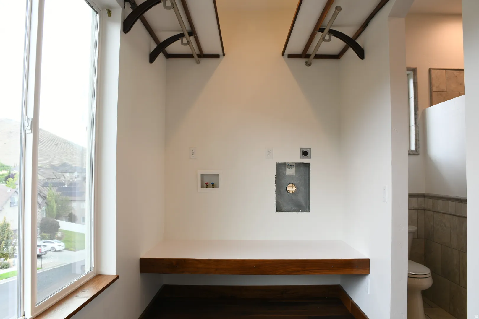Laundry area featuring a large window, built-in wooden countertop, wall-mounted drying racks, and connections for appliances
