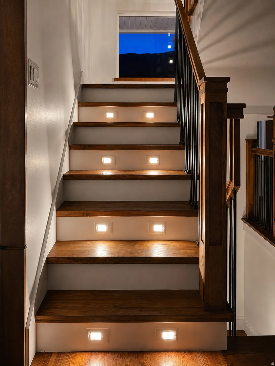 Hardwood staircase with integrated step lighting, a wood newel post, and black metal balusters