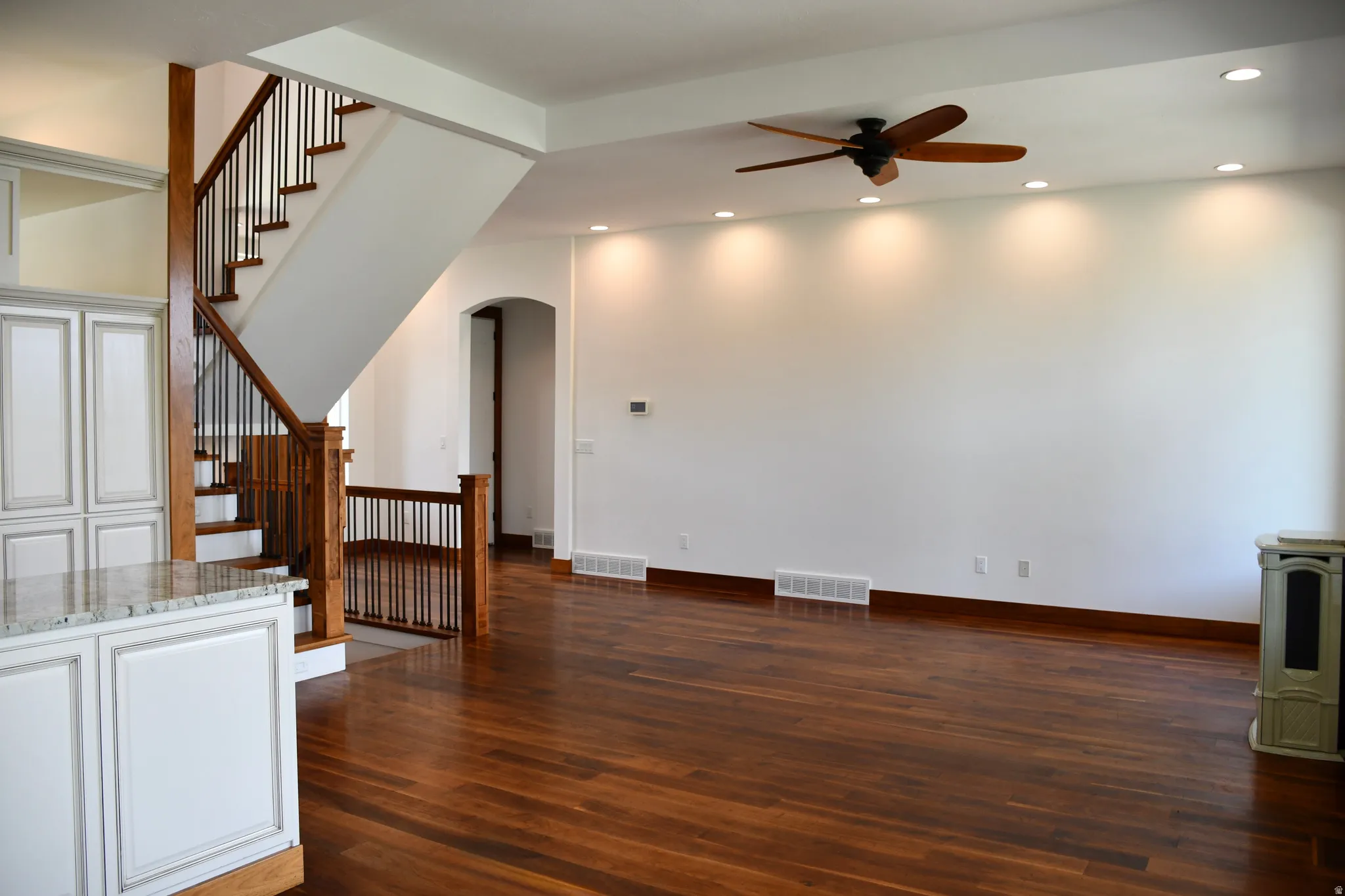 Hardwood flooring throughout, a staircase with wood newel posts and iron balusters, recessed lighting, a ceiling fan, and a built-in kitchen island with a stone countertop