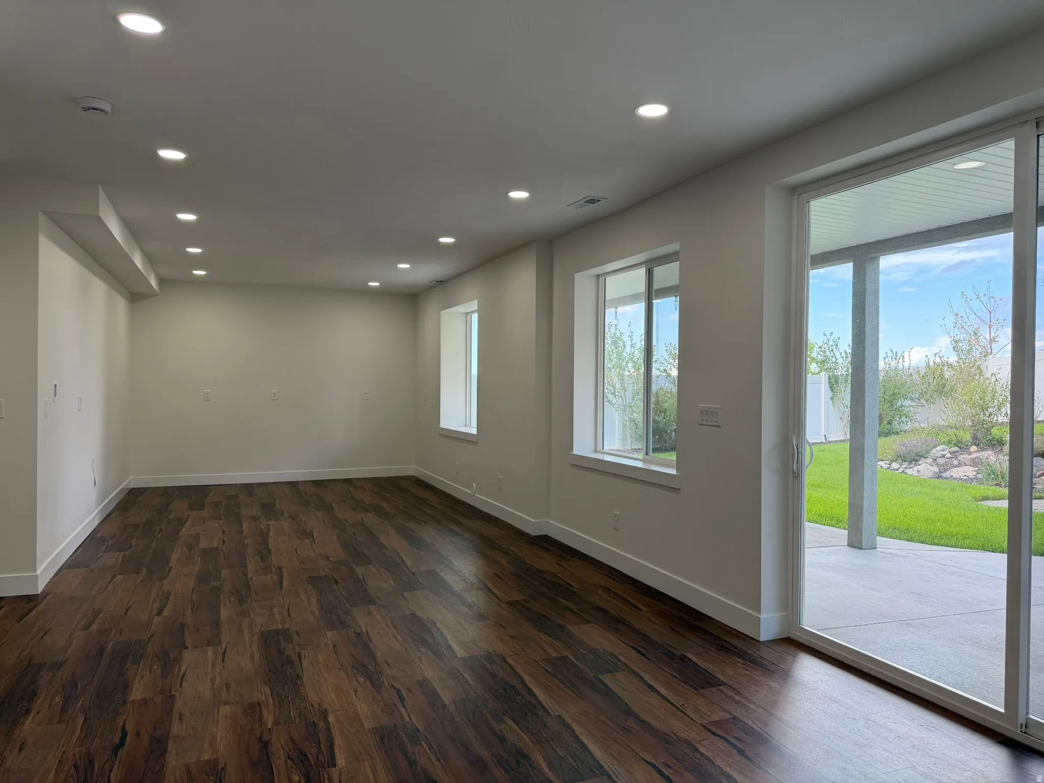 Spacious room featuring wood-finish flooring, recessed ceiling lighting, a large sliding glass door, and multiple windows
