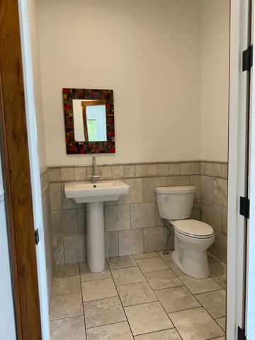 Pedestal sink, ceramic tile flooring, ceramic tiled wainscoting, white toilet, and wood-finish door frame