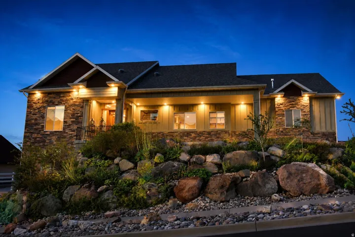 Stone and siding exterior with a gabled roofline, featuring decorative railings and a rock-lined landscape