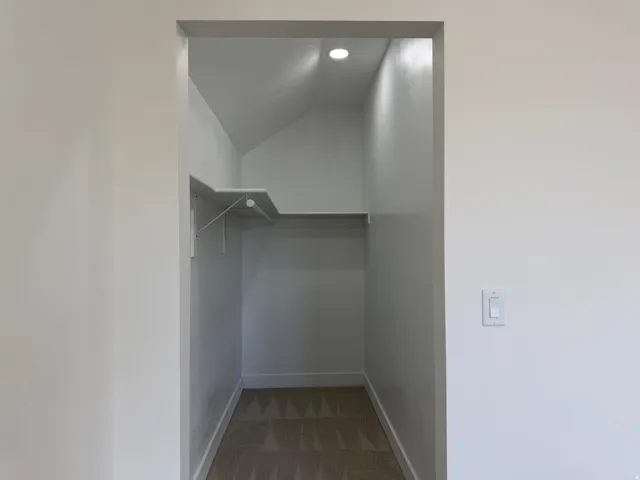 Recessed lighting illuminates a carpeted closet with built-in shelving and a clothing rod