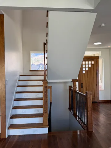 Wood-finish flooring, staircase with wood treads and white risers, wooden newel posts, and decorative metal balusters