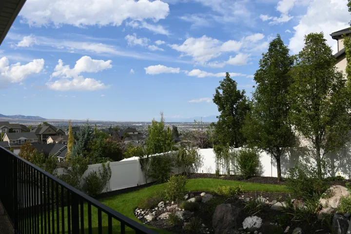 Landscaped backyard featuring a manicured lawn, established trees, and a white privacy fence