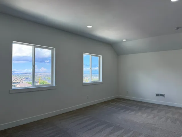Two expansive windows with white trim, vaulted ceiling, recessed lighting, and patterned carpeting