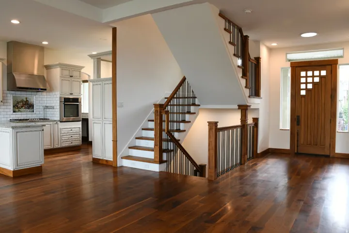 Hardwood flooring throughout, custom wood entry door, open-tread staircase with wrought iron balusters, recessed lighting, and kitchen with white cabinetry and stainless steel appliances