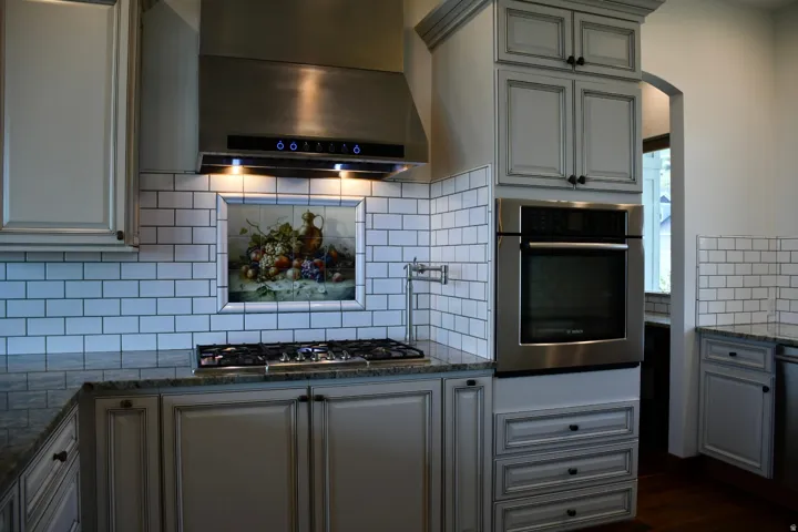 Stainless steel range hood, built-in wall oven, gas cooktop, subway tile backsplash, and granite countertops