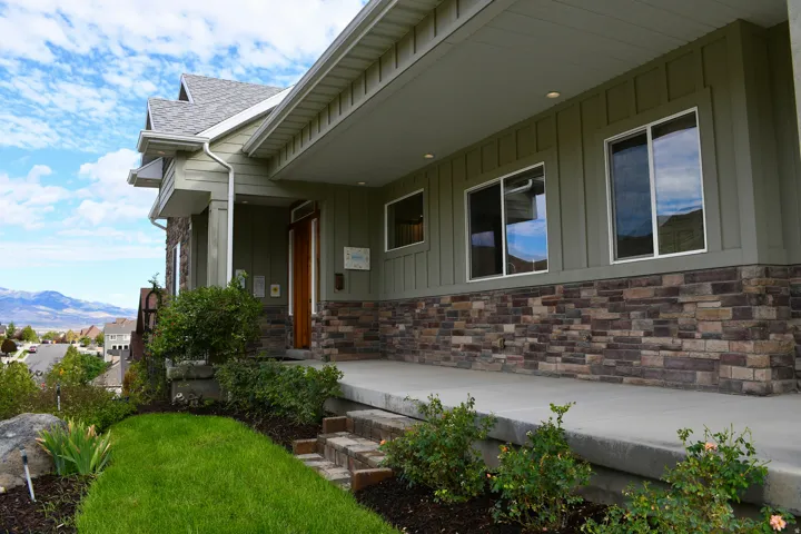 Covered front porch with stone veneer accent siding, vertical board siding, and multiple windows