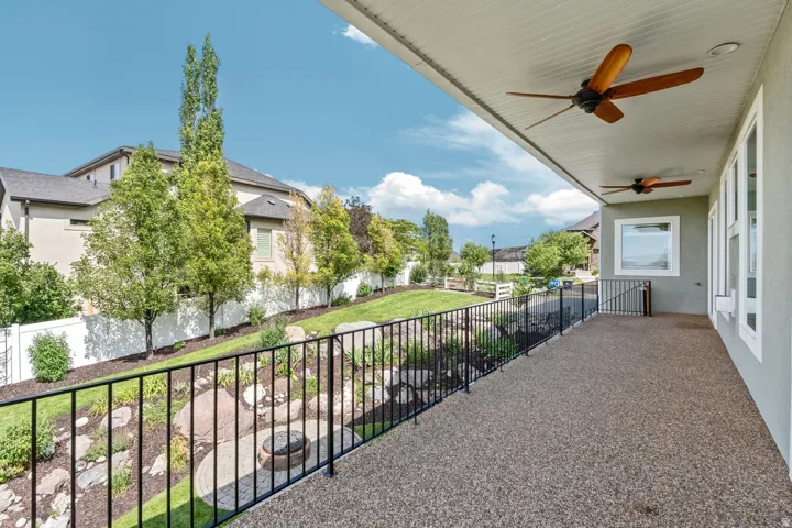 Expansive covered patio featuring a textured aggregate surface, two ceiling fans with wood-finish blades, and white trim windows