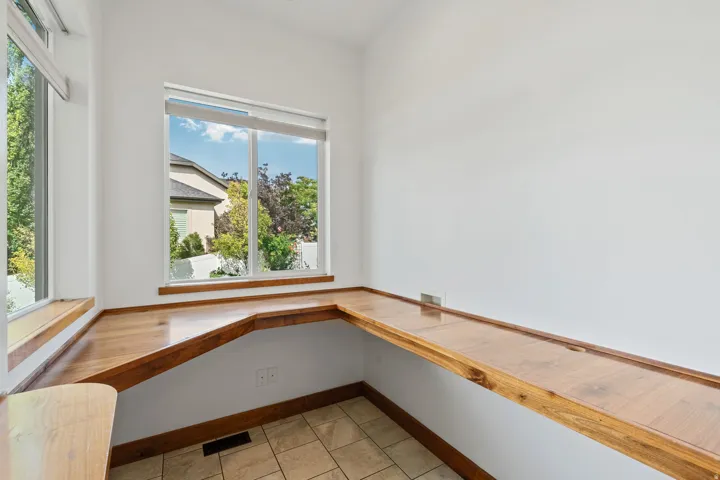 Built-in wood-finish desk with an L-shaped configuration, multiple windows, and tile flooring