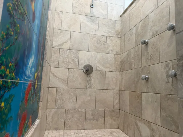 Tiled shower stall featuring body spray fixtures, a rainfall shower head, and a mosaic tile floor