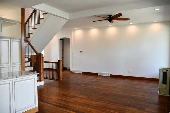 Hardwood flooring throughout, a staircase with wood newel posts and iron balusters, recessed lighting, a ceiling fan, and a built-in kitchen island with a stone countertop