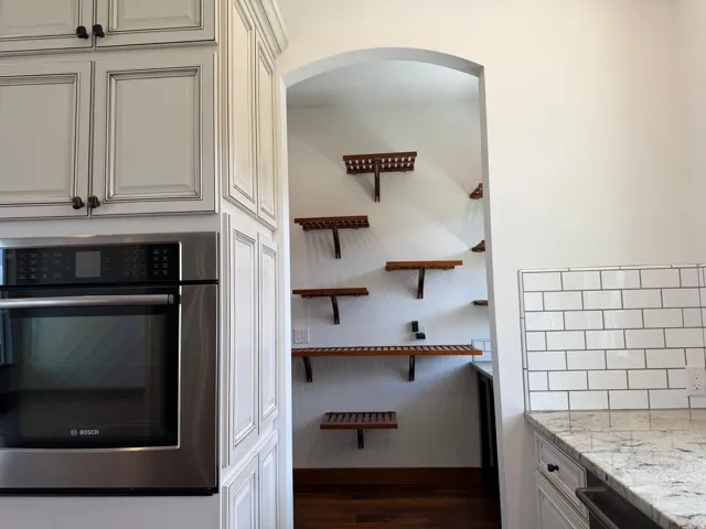 White paneled cabinetry, stainless steel built-in oven, granite countertop, white subway tile backsplash, and an arched doorway