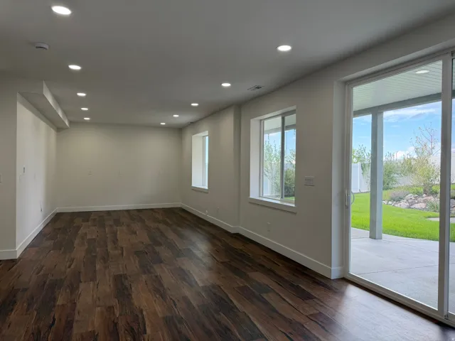 Spacious room featuring wood-finish flooring, recessed ceiling lighting, a large sliding glass door, and multiple windows