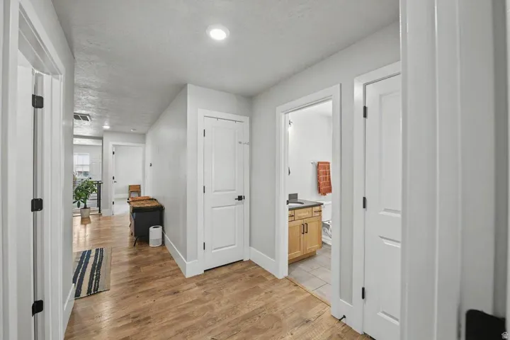 Hallway featuring wood-finish flooring, recessed lighting, white trim, and doors with black hardware