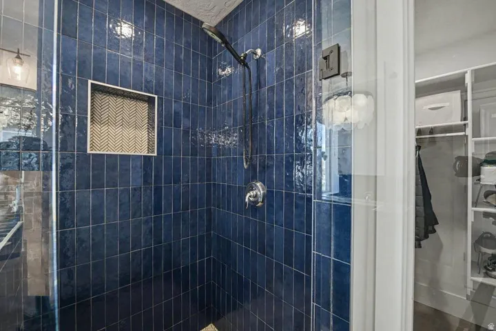 Shower enclosure featuring dark blue rectangular wall tiles, a built-in niche with herringbone tile, and a chrome shower head and controls