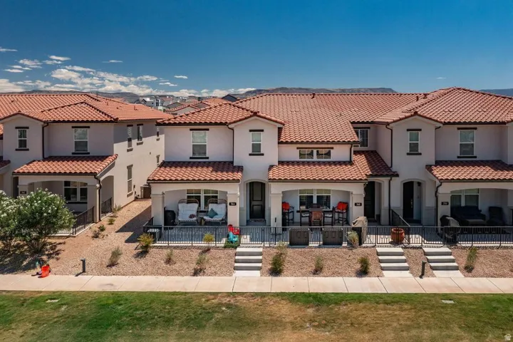 Exterior featuring multi-story stucco construction, terracotta roof tiles, individual covered patios, front entry staircases, and a low-maintenance xeriscaped front yard