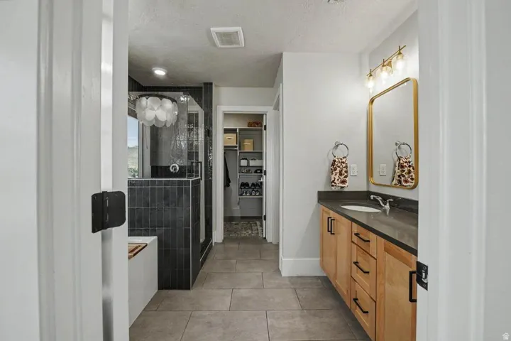 Bathroom featuring a light wood-finish vanity with dark countertops, an undermount sink, and a framed mirror with overhead lighting