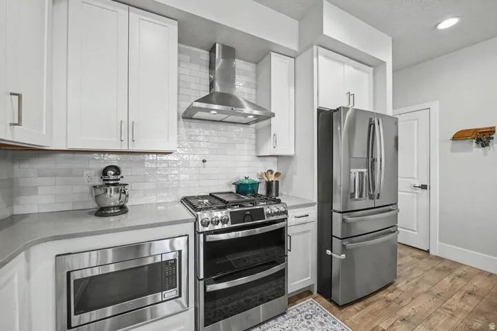 Modern kitchen featuring white shaker cabinetry, stainless steel appliances, light-toned countertops, a subway tile backsplash, and wood-finish flooring