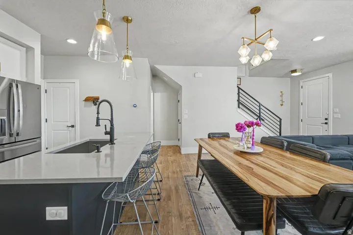 Open-concept living area featuring a kitchen island with integrated sink, wood-finish flooring, a modern dining table, and a staircase with metal railings