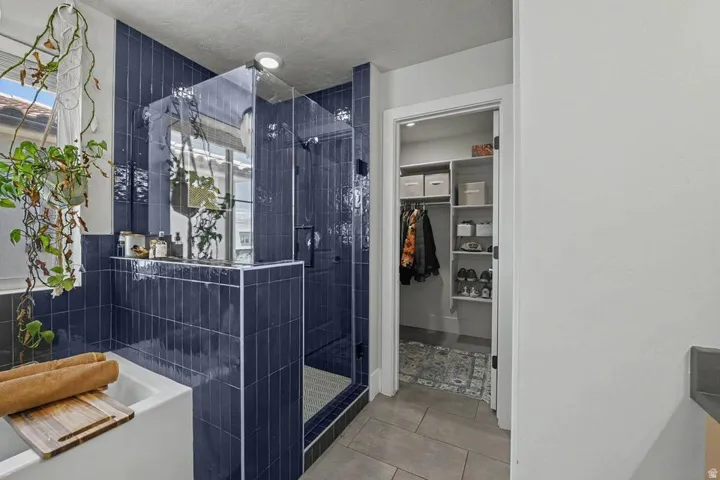 Bathroom featuring a deep soaking tub, glass-enclosed shower with dark tile surround, and a custom built-in closet with shelving