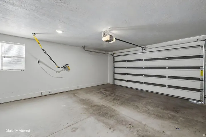 Spacious garage featuring a concrete floor, overhead lighting, and a window with horizontal blinds