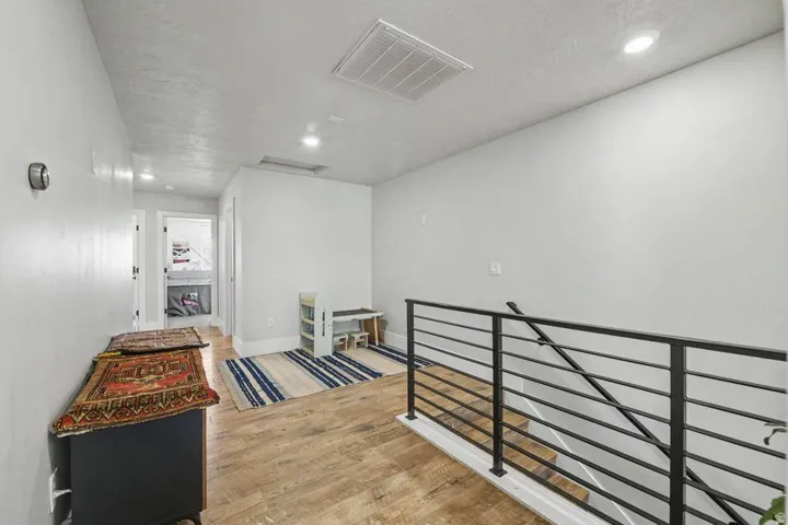 Upper-level landing featuring wood-finish flooring, a contemporary metal railing, recessed ceiling lighting, and a visible hallway entrance