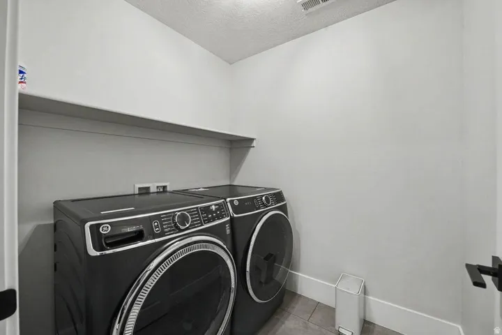 Dedicated laundry area featuring a wall-mounted shelf, light gray walls, and tile flooring