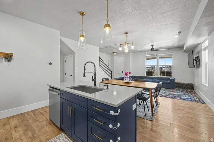 Open-concept living space featuring wood-finish flooring, a kitchen island with a built-in sink and dishwasher, a quartz-look countertop, and contemporary pendant lighting