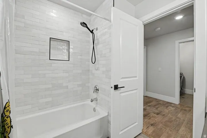 Bathtub and shower combination featuring white subway tile surround, recessed shower niche, and matte black shower head
