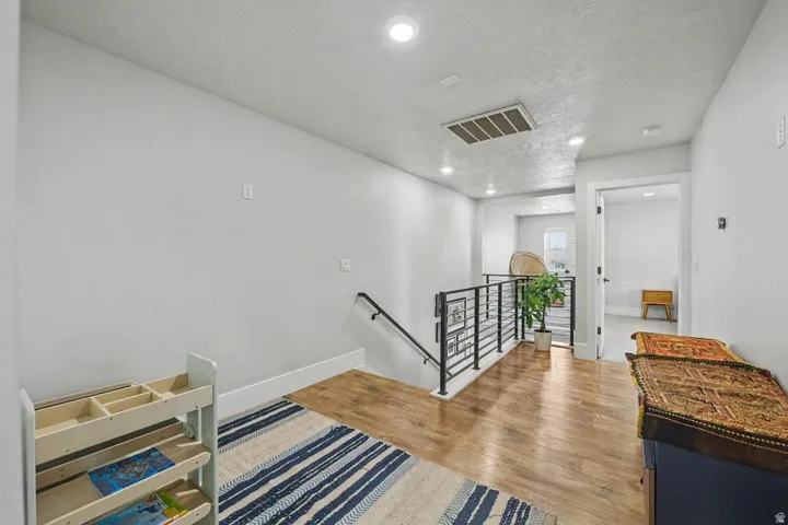 Open hallway featuring wood-finish flooring, recessed lighting, and a contemporary black metal balustrade