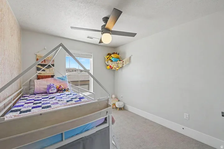 Bedroom featuring a textured accent wall, light gray carpet, and a modern ceiling fan with integrated lighting