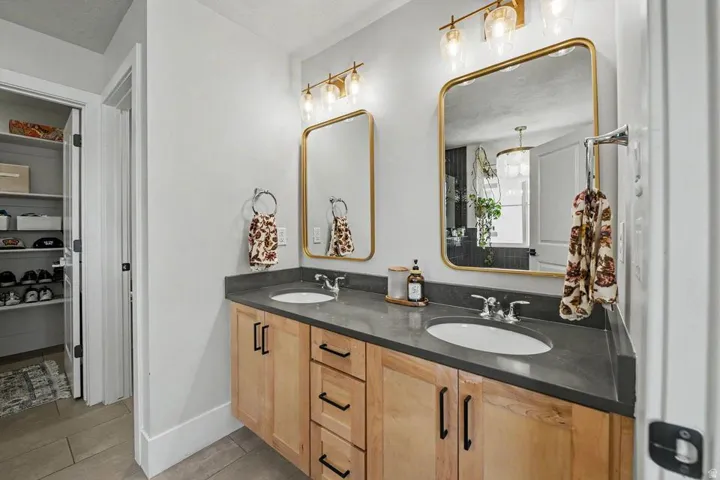 Double vanity featuring light wood-finish cabinetry and a dark countertop with dual undermount sinks