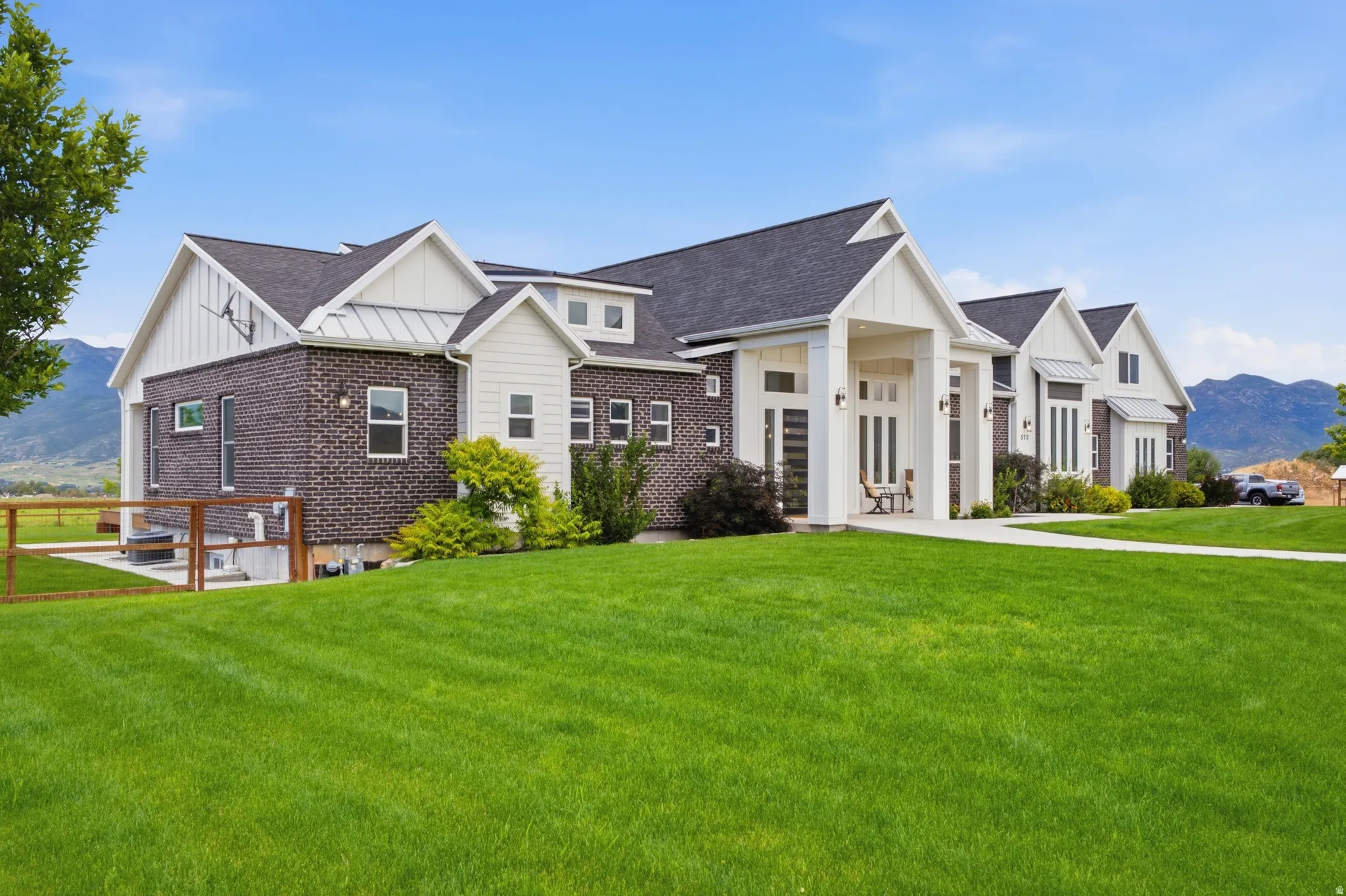 Modern ranch-style home featuring a dark brick facade, white vertical siding accents, a prominent covered entry with columns, multiple gables, and a wide front lawn