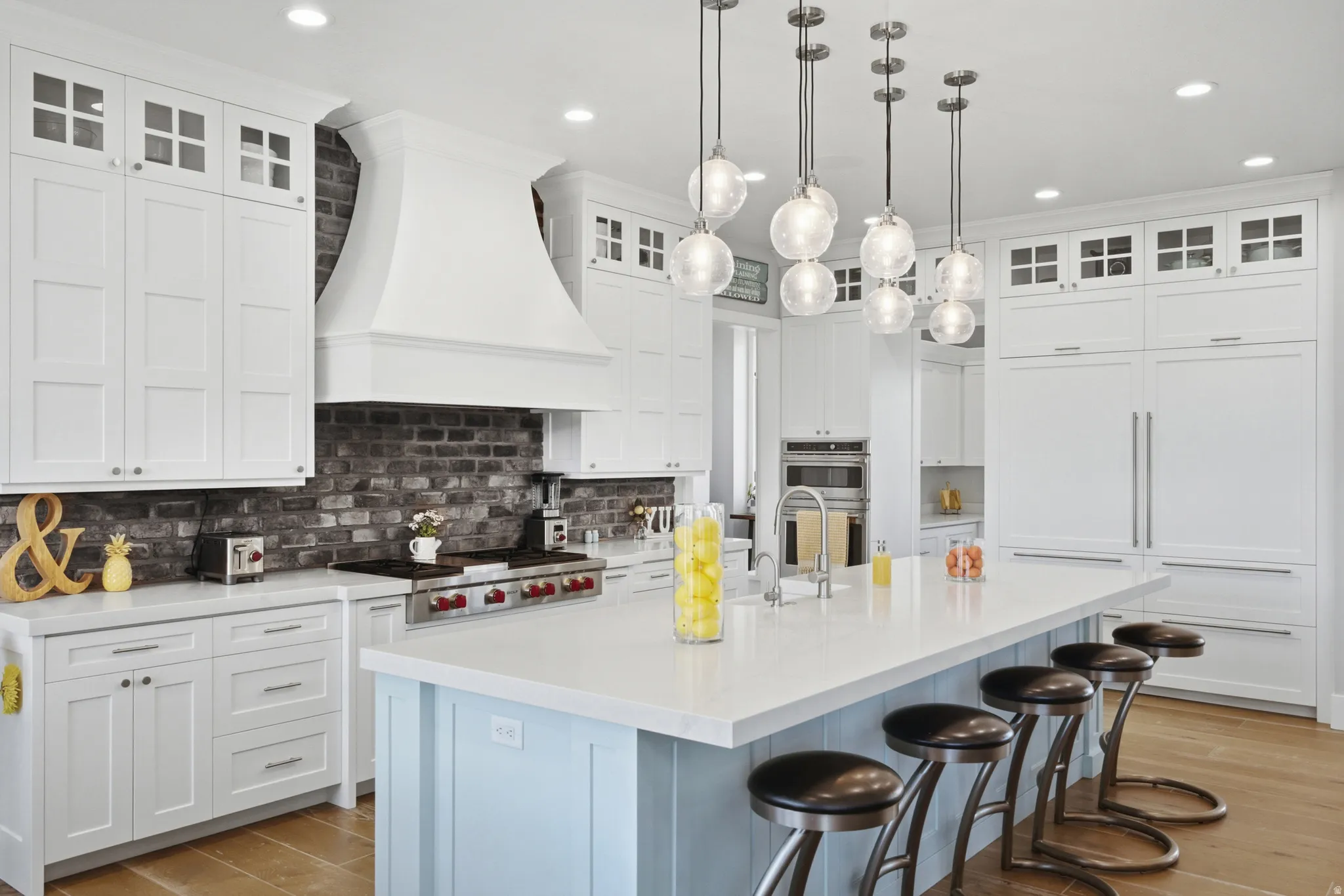 Gourmet kitchen featuring a large island with seating, a professional-grade range with a custom hood, integrated paneled appliances, a dark brick backsplash, and wood-finish flooring