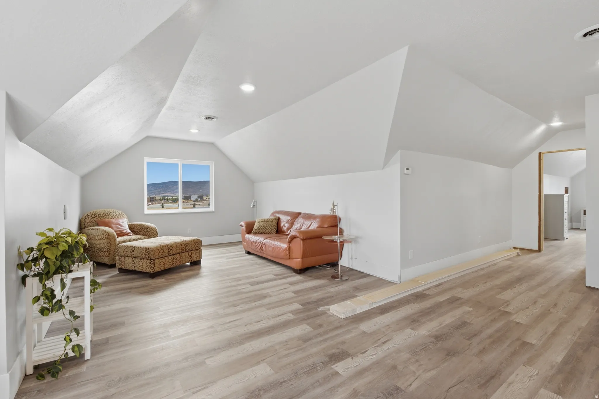 Spacious open room featuring a large window, wood-finish flooring, recessed lighting, and sloped ceilings