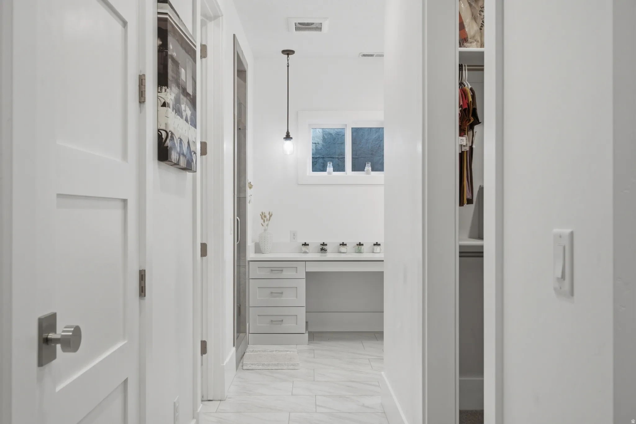 White bathroom vanity with built-in desk, under-mount sink, and contemporary pendant lighting