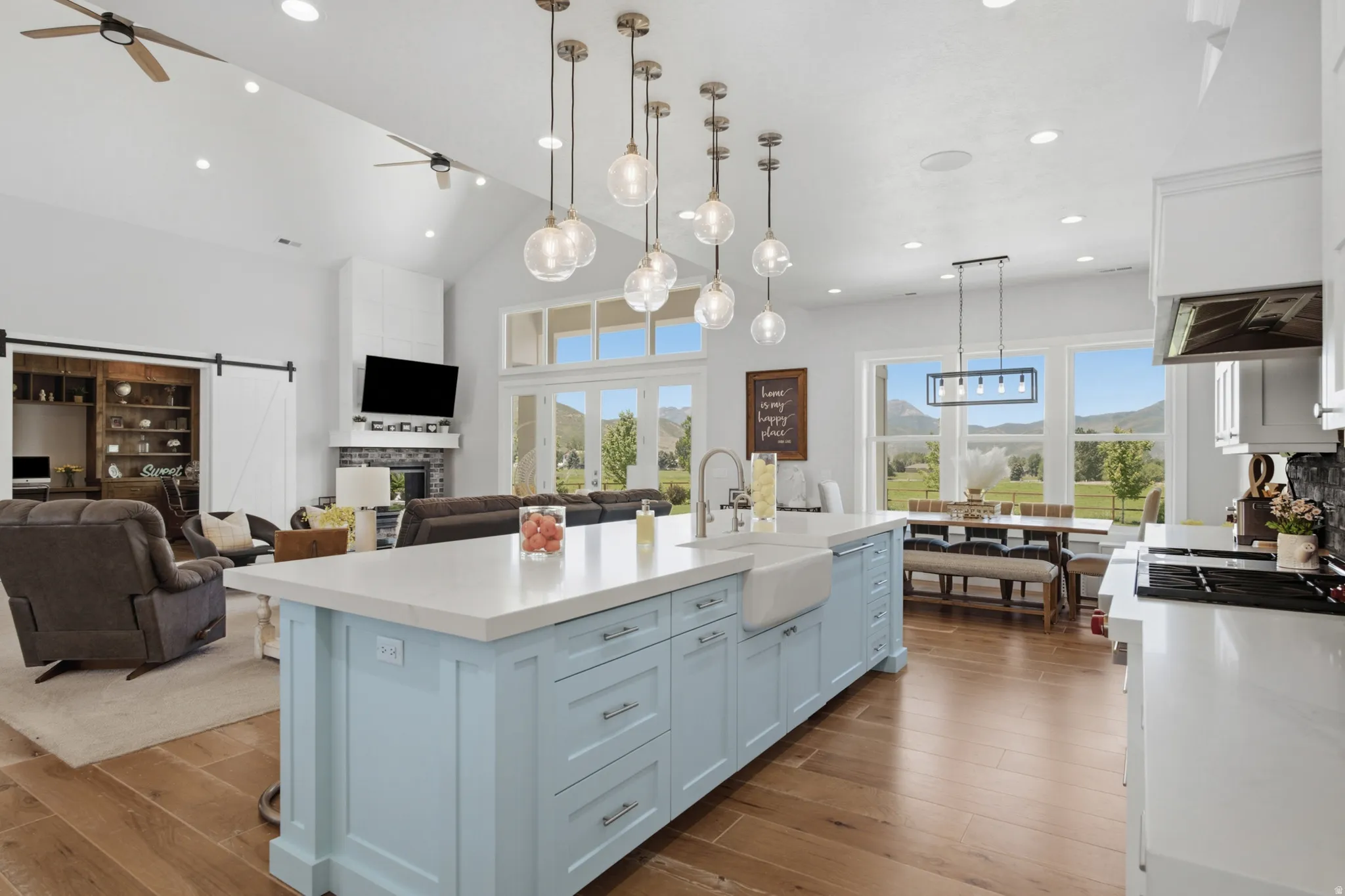 Spacious kitchen featuring a light blue island with a farmhouse sink and pendant lighting, white cabinetry, and wood-finish flooring