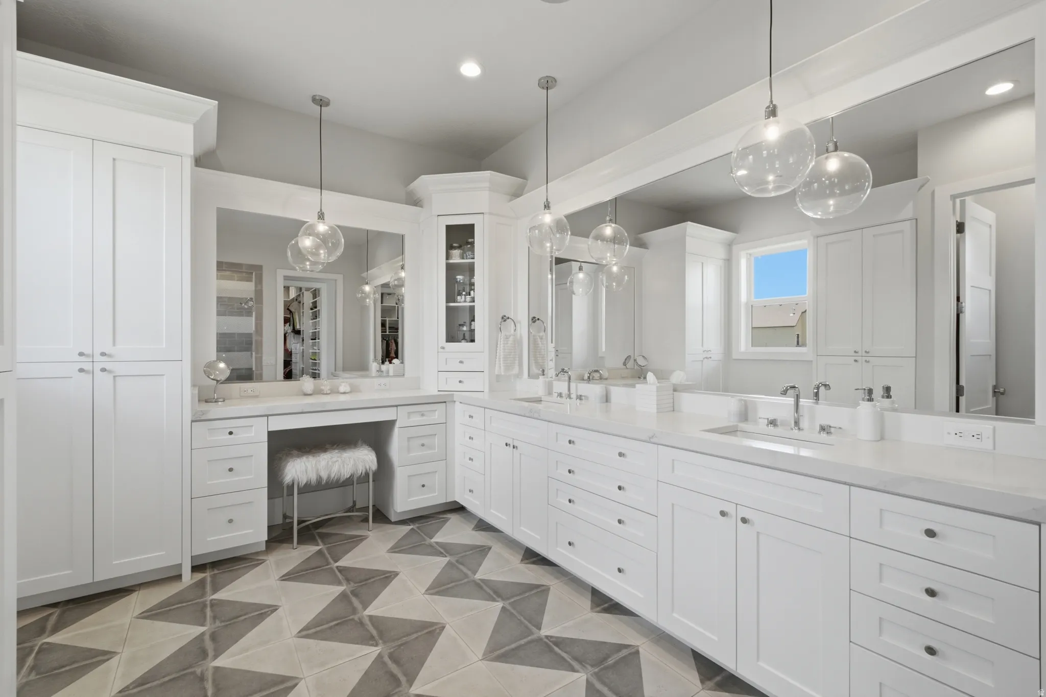Expansive vanity area featuring dual sinks set in a white countertop, extensive white cabinetry, and a dedicated vanity with a large mirror