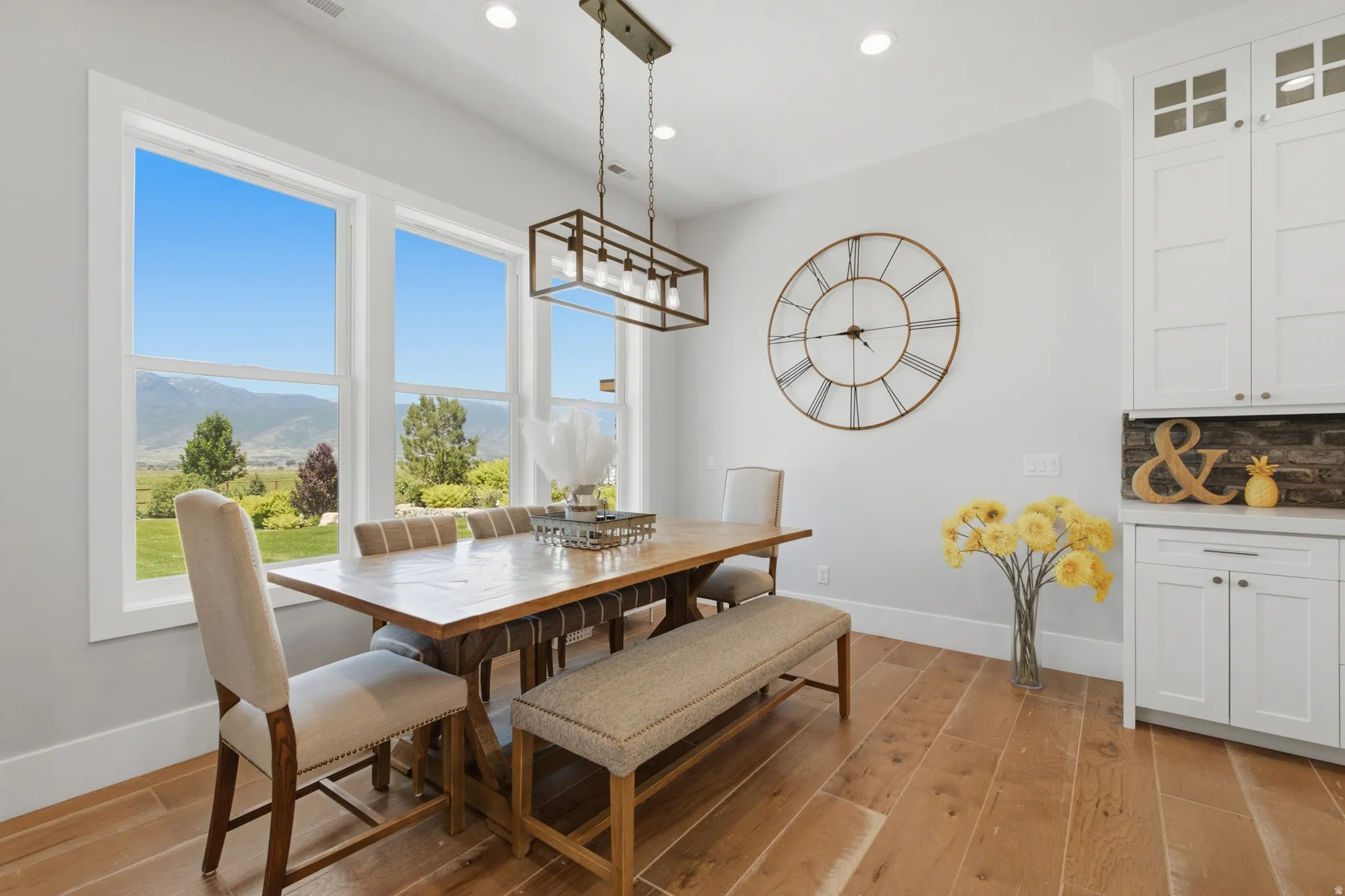 Dining area featuring large windows showcasing mountain scenery, wood-finish flooring, a contemporary chandelier, white built-in cabinetry, and a stone-effect backsplash