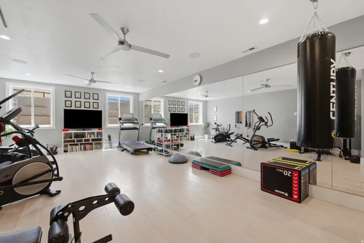 Dedicated fitness space featuring light wood-finish flooring, full-wall mirrors, recessed lighting, and multiple ceiling fans