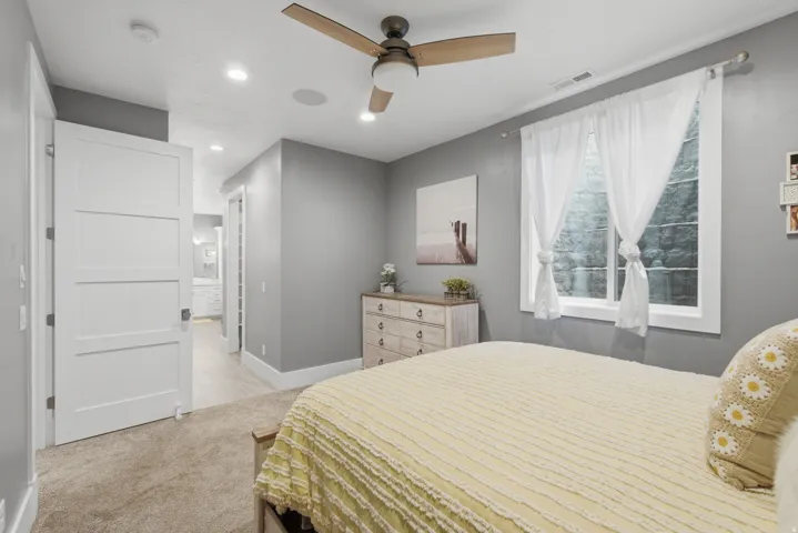 Neutral-toned bedroom with a wood-finish ceiling fan, recessed lighting, and a window with white trim